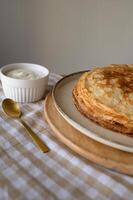 A stack of golden pancakes, served with a bowl of sour cream , beautifully arranged on a rustic table. photo