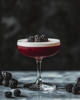 Refreshing blackberry bramble cocktail garnished with fresh blackberries on marble table photo