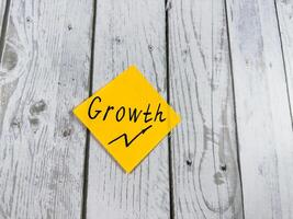 Sticky note featuring the word Growth with an upward arrow, set against a rustic textured wooden surface, symbolizing development, optimism, and the pursuit of personal and professional advancement photo