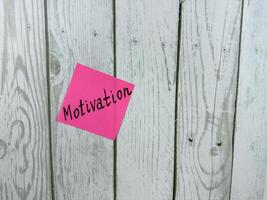Pink sticky note with the word Motivation written on it, pinned on a white wooden board background. The image symbolizes inspiration, drive, and determination. Excellent for concept themes photo