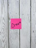 Bright pink sticky note featuring the word Dream placed on a textured wooden background, symbolizing aspirations, creativity, and the pursuit of one's deepest desires and goals photo