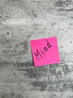 Bright pink sticky note displaying the word Mind against a textured grey surface, symbolizing mental focus, awareness, and the importance of mindfulness in everyday life photo