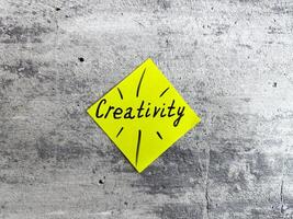 Vibrant yellow sticky note shaped as a diamond displaying the word Creativity and decorative elements on a textured grey background, representing the essence of innovative thinking and inspiration photo