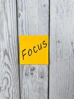Sticky note with Focus written on it, placed on white wooden board. Ideal for conveying themes of concentration, proactive mindset, productivity, and goal achievement photo