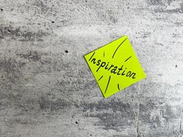 Bright yellow sticky note shaped as a diamond featuring the word Inspiration and decorative elements on a textured grey background, symbolizing the power of motivating ideas and creativity photo
