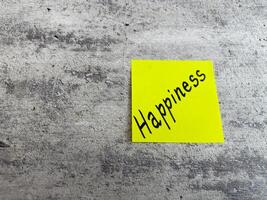Vivid yellow sticky note displaying the word Happiness against a textured grey background, symbolizing the importance of joy and positivity in everyday experiences and personal growth photo