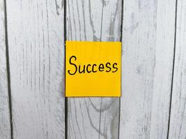 Bright sticky note displaying the word Success against a rustic textured wooden background, symbolizing achievement, personal growth, and the journey toward goals photo