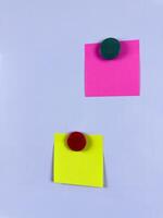 Pink and yellow sticky notes secured with magnets on a whiteboard ideal for reminders planning and organization in office school or home environments enhancing efficiency and creativity photo