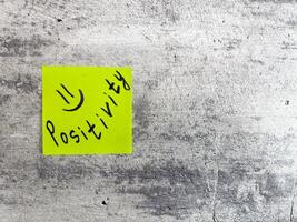 Sticky note displaying the word Positivity along with smiley face on a textured grey surface, embodying the spirit of optimism and the importance of a positive attitude in everyday life photo
