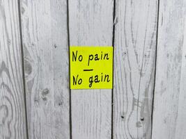 Bright yellow sticky note with the phrase No pain No gain written on it, pinned on white wooden board background. Image symbolizes motivation, effort, and perseverance. Great for concept themes photo