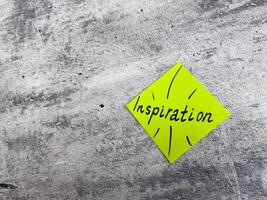 Vibrant yellow sticky note in a diamond shape displaying the word Inspiration with decorative elements on textured grey surface, representing the essence of motivating ideas and creative potential photo