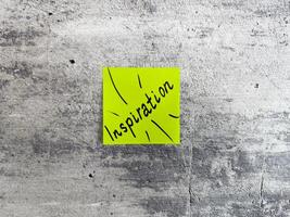 Vibrant yellow sticky note shaped as a rectangle displaying the word Inspiration with decorative rays on a textured grey background, acting as a symbol of creativity and motivating ideas photo