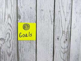Sticky note showcasing the word Goals accompanied by target symbol, set against textured wooden background, symbolizing the importance of setting and achieving personal aspirations photo