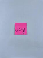 Sticky note with the word Joy written on it, placed on white background. Ideal for illustrating themes of happiness, positivity, and delight. Great for concept creation photo