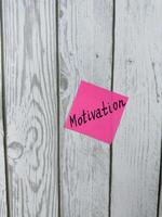 Pink sticky note with the word Motivation written on it, placed on a white wooden background. Ideal for themes of inspiration, determination, and achieving goals. Perfect for motivation concept photo