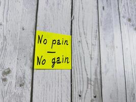 Yellow sticky note with No pain No gain written on it, placed on wooden board. Photo symbolizes hard work and perseverance, ideal for encouraging themes of motivation and effort