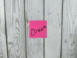 Pink sticky note displaying the word Dream against wooden background, representing the essence of aspirations, imagination, and the pursuit of personal goals and dreams photo