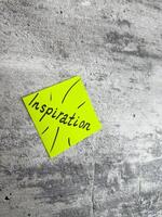 Bright yellow sticky note in a diamond shape featuring the word Inspiration and decorative rays on a textured grey background, symbolizing the spark of creativity and motivating ideas photo
