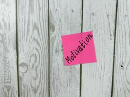 Pink sticky note with Motivation written on it, placed on a white wooden board. This image symbolizes motivation and commitment, ideal for conveying themes of drive and determination photo