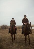 Young romantic couple horse riding, against the background of a field with autumn grass. galloping across the fields, stylishly dressed in brown shades. smiling during a romantic honeymoon photo