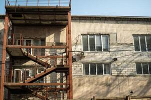 Industrial building with brown iron external staircase. The building has white plastic windows. The building is made of brick, slabs and tiled. A large brick building with many windows.. photo