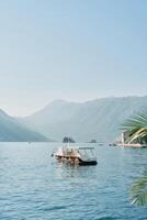 View from the shore of a tourist boat sailing on the sea towards the mountains photo