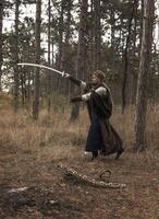 art photo of a warrior girl with a sword in her hands. blonde dressed in a historical costume of a warrior woman, training with a sword in her hands. dressed in a long cloak. warrior raised a sword