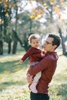 Dad is talking to a little girl in his arms in a sunny park photo