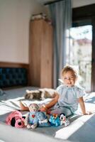 Teddy bear and soft toys sit in a row on the bed against the background of a little smiling girl photo