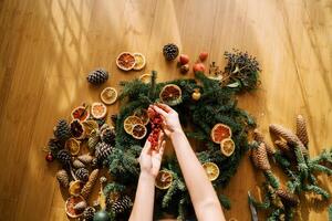 Female hands hold a sprig of red berries over a Christmas wreath lying on the floor. Top view photo
