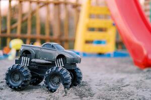 Toy Bigfoot jeep stands on the sand at a colorful playground photo