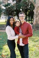 Smiling mom hugging dad with a little girl in his arms in the park photo