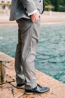 Man stands with his hands in his trouser pockets on the pier near the bollard. Cropped. Faceless photo
