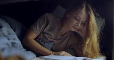 A contemplative young woman is reading in her bed, surrounded by the warmth of soft light video