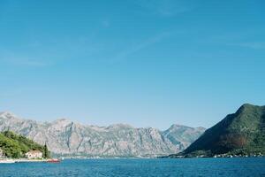 Red boat sails on the sea against the backdrop of a high mountain range photo
