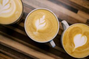 Cups of cappuccino with patterns on the foam stand diagonally on a wooden table. Top view photo