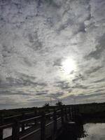a bridge over a body of water with the sun shining through the clouds photo