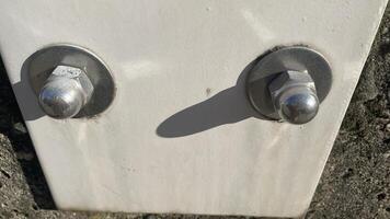 Close-up view of bolts securing a white metal plate to a textured stone wall in bright daylight photo