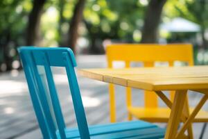 Colorful outdoor seating with turquoise and yellow chairs beside a wooden table in a park setting photo