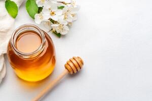 Natural honey in jar with wooden dipper and fresh flowers on light background photo