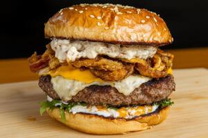 Gourmet burger stacked with cheese, crispy onions, and special sauce on a wooden platter photo