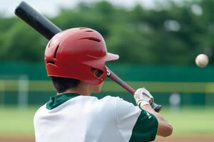 Young batter in red helmet prepares to swing at baseball during practice on a sunny afternoon photo