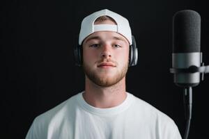 Young man recording music in a studio with headphones and a microphone against a dark background photo