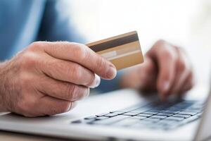 User engages in online shopping with credit card in hand while sitting at laptop desk photo