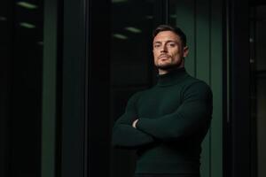 Confident man poses in a sleek urban setting during evening hours with modern architecture and soft lighting photo