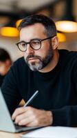 Focused man working on laptop in modern cafe while taking notes during midday hours photo