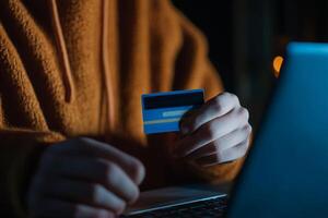 Person holding a credit card while making an online purchase at night in a dimly lit room photo