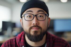 Portrait of a man wearing a beanie and glasses, smiling in a modern workspace during daytime photo