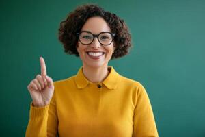 Teacher in a bright yellow sweater smiles while raising her finger in a classroom setting at daytime photo