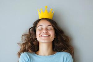 Young woman wearing a yellow crown smiles joyfully against a neutral background at a relaxed indoor setting photo